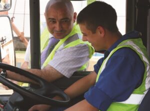 A LGV learner driver sitting in a lorry cab with an instructor showing him what to do