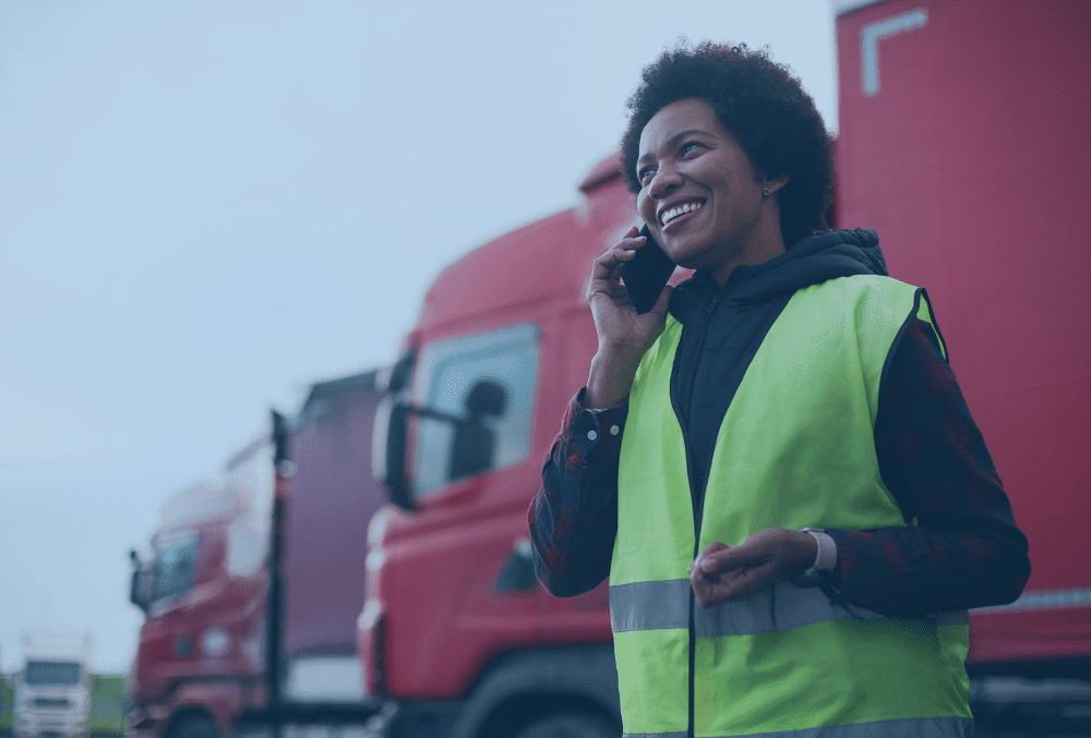Woman transport manager speaking on a mobile phone in a yellow hi vis jacket infront of some red lorries